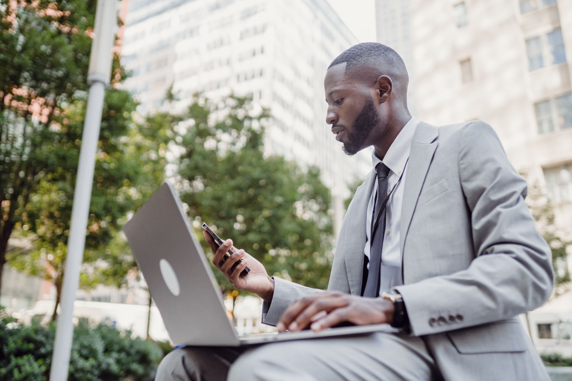 Businessman in a suit using a laptop and smartphone in an urban setting, blending technology with business. — Creating Memora