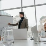 Professionals engaged in a collaborative business meeting with charts and laptops in a modern office setting. — Danish Televi