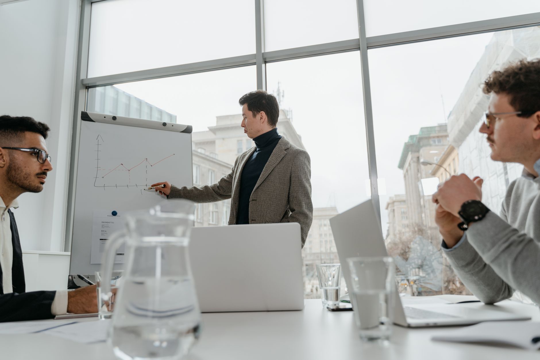 Professionals engaged in a collaborative business meeting with charts and laptops in a modern office setting. — Danish Televi