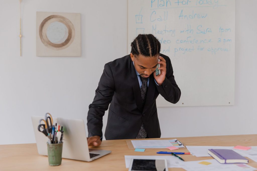 Professional businessman multitasking with phone and laptop at office desk, surrounded by documents. — Gary Guglielmo: Your G