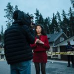 A female journalist reports live from an outdoor crime scene, flanked by police officers and media personnel. — Get Your Favo