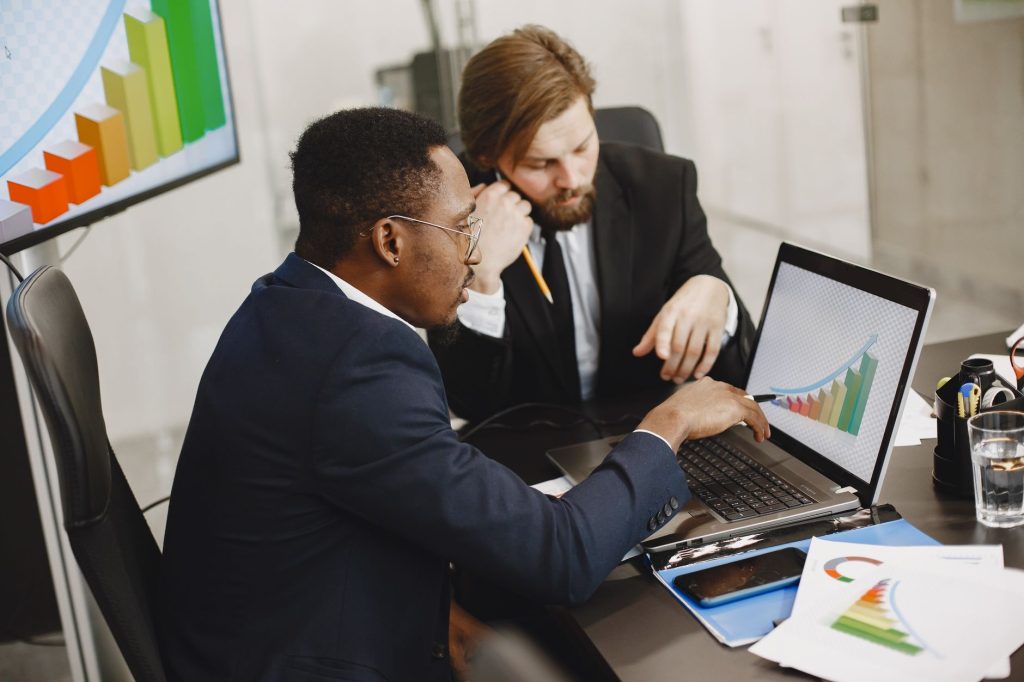 Two business professionals working on growth charts using laptop in an office setting. — How COLA Adjustments Improve Retirem
