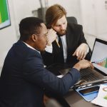 Two business professionals working on growth charts using laptop in an office setting. — How COLA Adjustments Improve Retirem