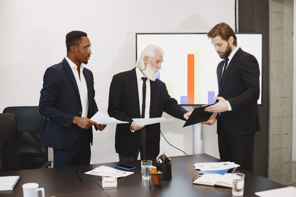 Three businessmen discussing documents in a conference setting with a presentation screen. — Leverage Qualified Opportunity Z