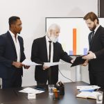 Three businessmen discussing documents in a conference setting with a presentation screen. — Leverage Qualified Opportunity Z