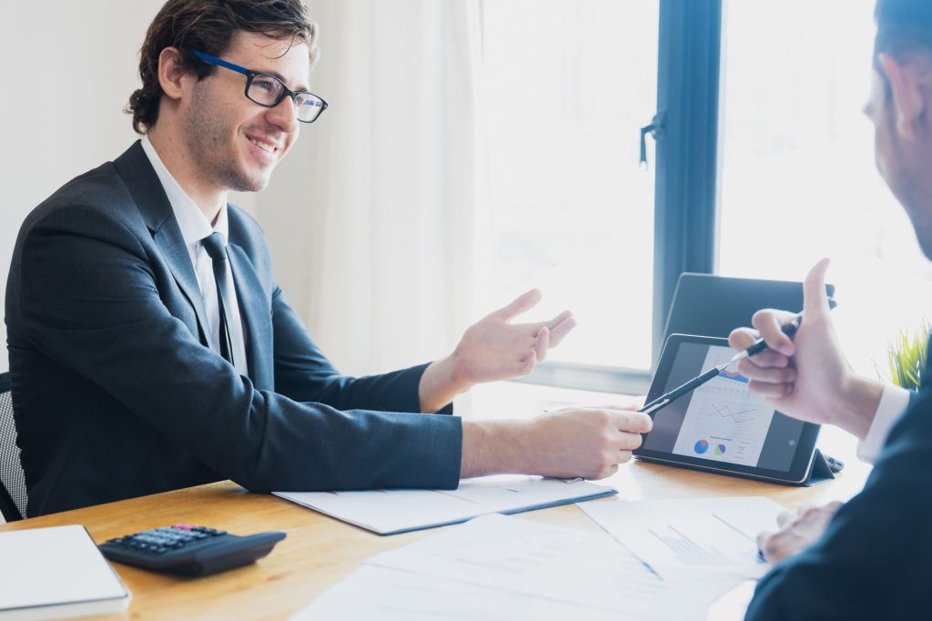 Two businessmen in formal attire discussing a business report in an office setting with a tablet. — Reddit Ringside: Explorin