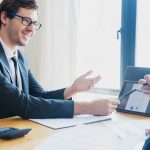 Two businessmen in formal attire discussing a business report in an office setting with a tablet. — Reddit Ringside: Explorin