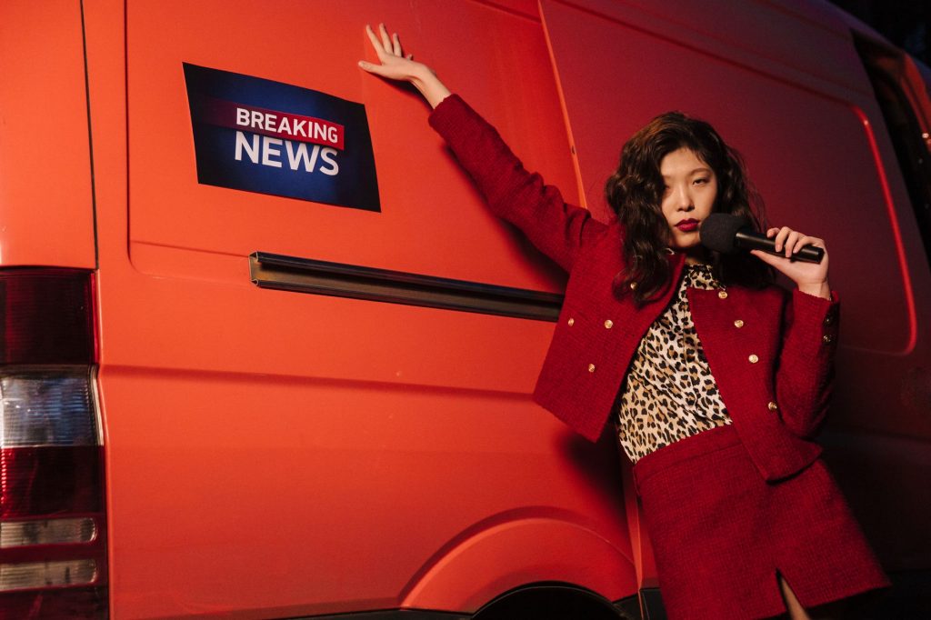 Fashionable reporter with microphone posing dramatically next to a news van. — The Ripple Effect of Koitoto Wins on Finances