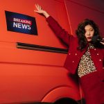 Fashionable reporter with microphone posing dramatically next to a news van. — The Ripple Effect of Koitoto Wins on Finances