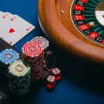 A close-up of poker chips, playing cards, and a roulette wheel on a blue background.